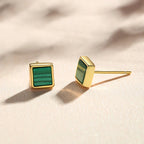 A pair of gold square stud earrings with a green striped inlay, shown on a light cream background.