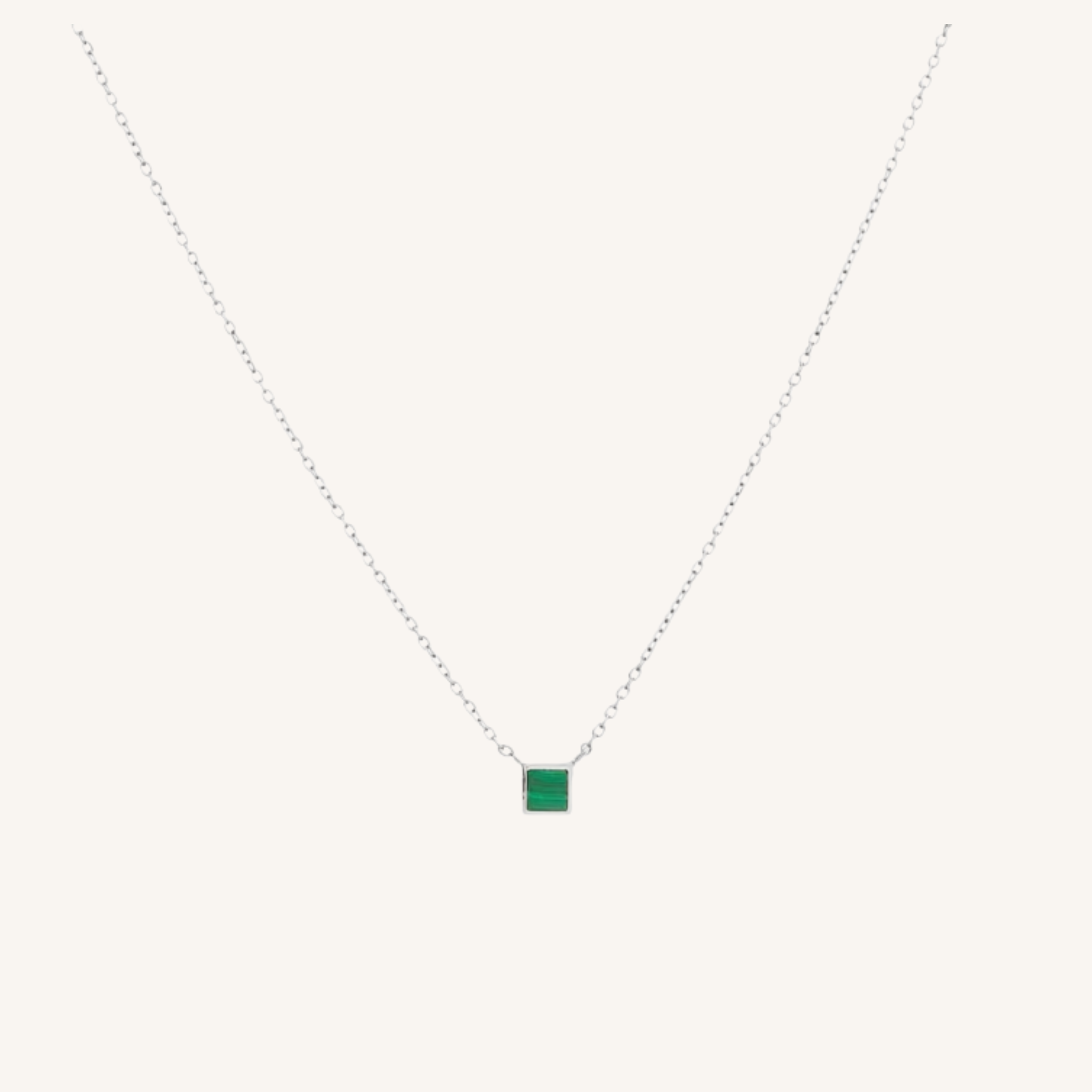 A delicate silver chain necklace featuring a small square green gemstone pendant, displayed against a solid off-white background.