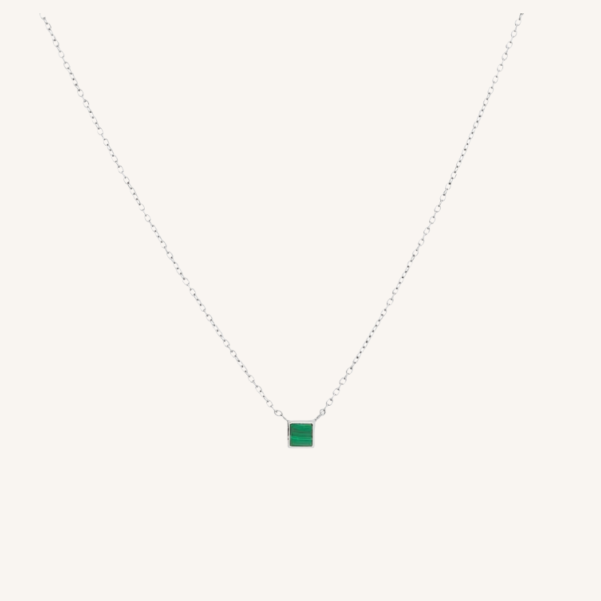 A delicate silver chain necklace featuring a small square green gemstone pendant, displayed against a solid off-white background.