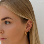 Close-up of a person wearing gold hoop earrings with a neutral background.