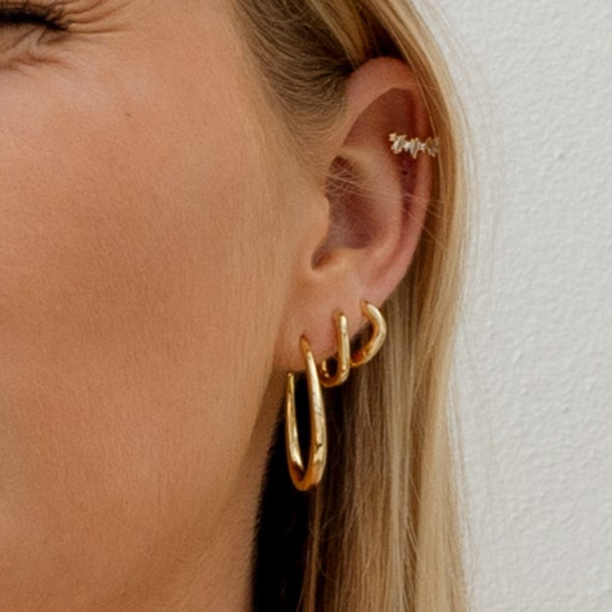 Close-up of an ear wearing gold hoop earrings with a plain background