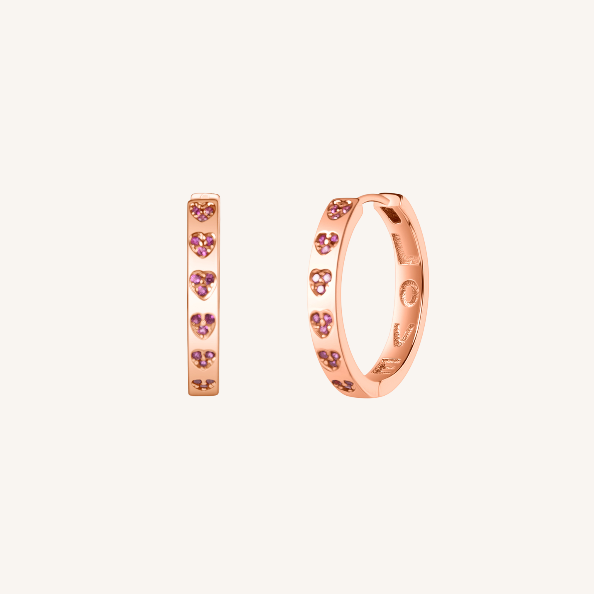 A pair of rose gold huggie hoop earrings decorated with small pink heart-shaped crystals, shown on a light cream background.