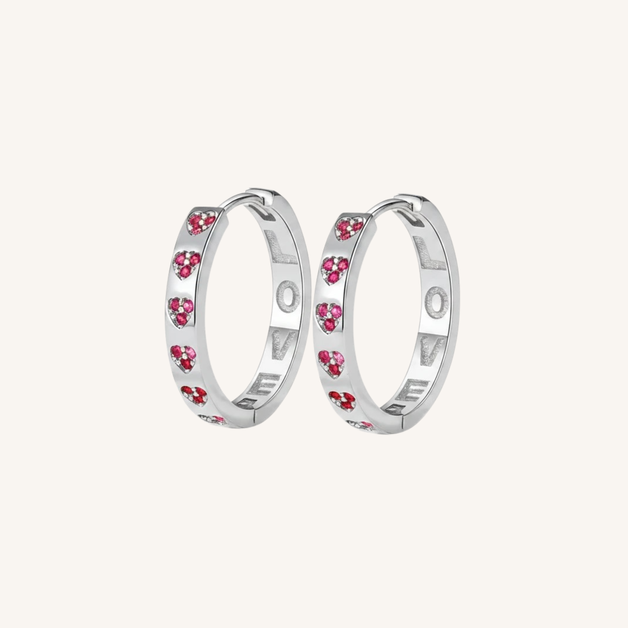A pair of silver hoop earrings with small pink heart-shaped crystals set along the outer band, shown against a solid off-white background.