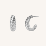 A pair of silver twisted hoop earrings shown on a plain off-white background, with one earring facing forward and the other angled to show the side profile and post.