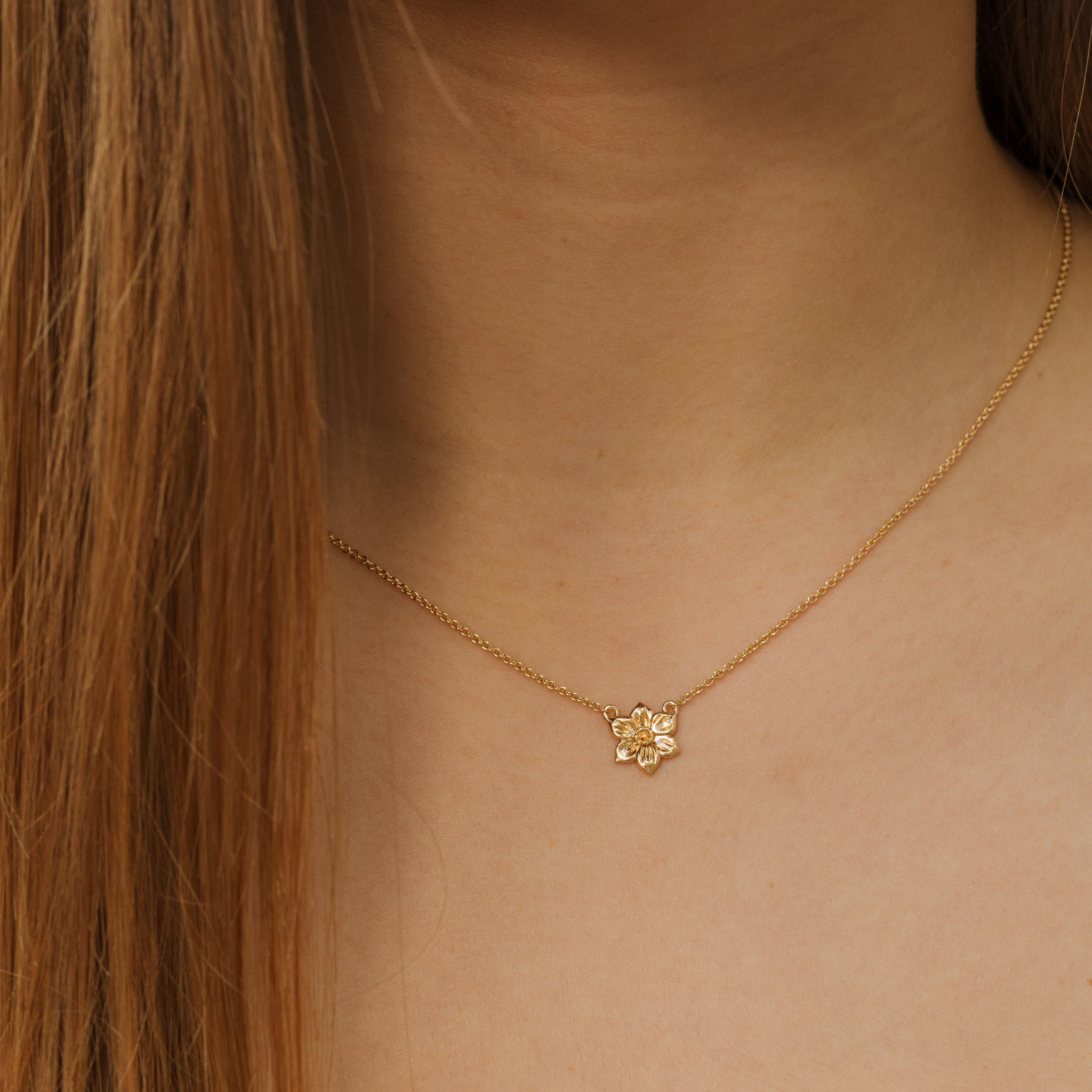 Gold necklace with a small flower pendant on a person's neck