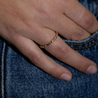 A close-up of a person's hand wearing a thin, textured rose gold band ring, resting on blue denim fabric.