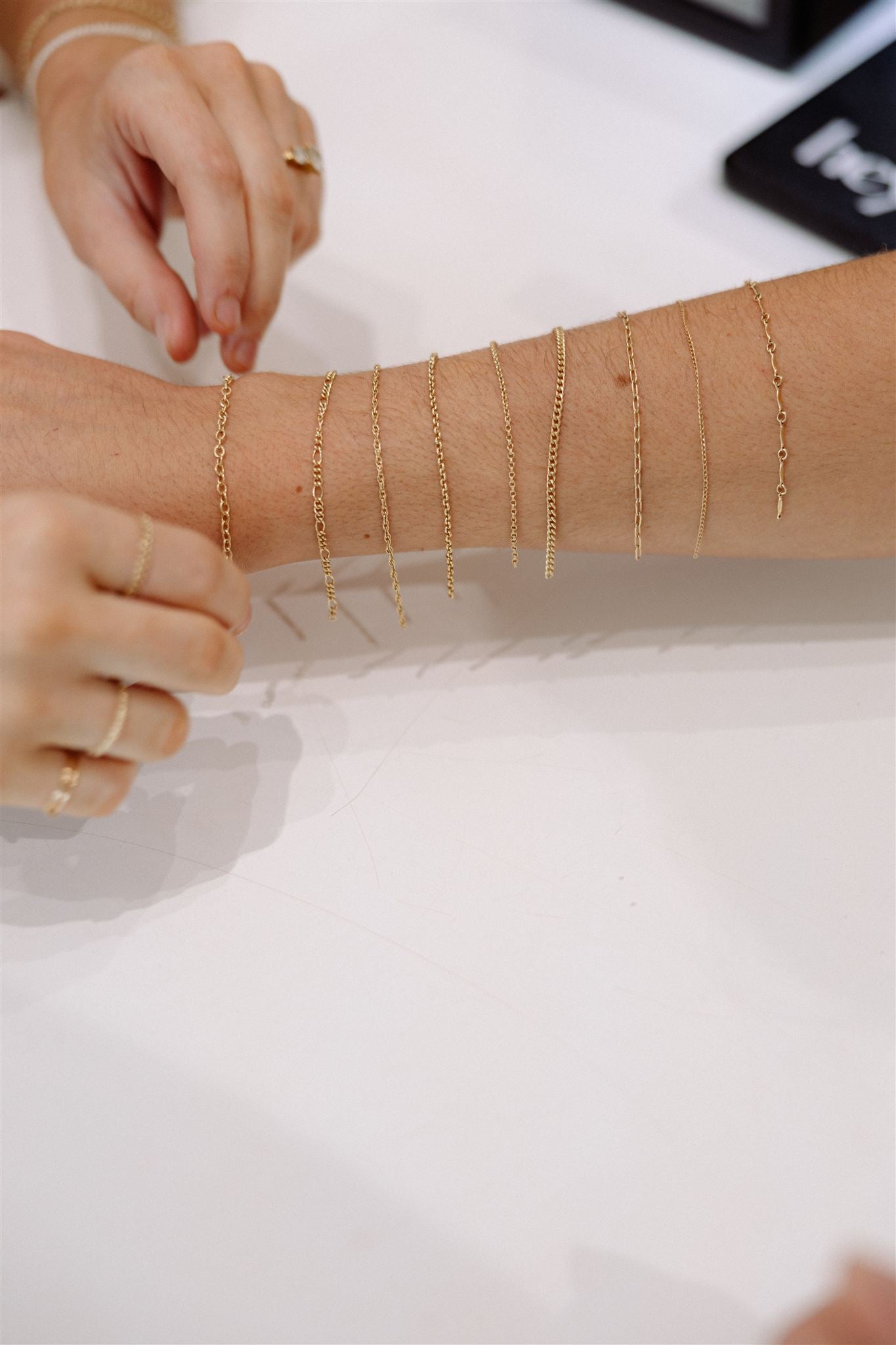 Gold chain necklaces being tried on a person's arm against a white background