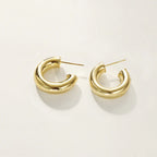 A pair of polished gold huggie hoop earrings, on a clean, off-white background.