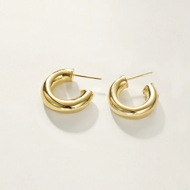 A pair of polished gold huggie hoop earrings, on a clean, off-white background.