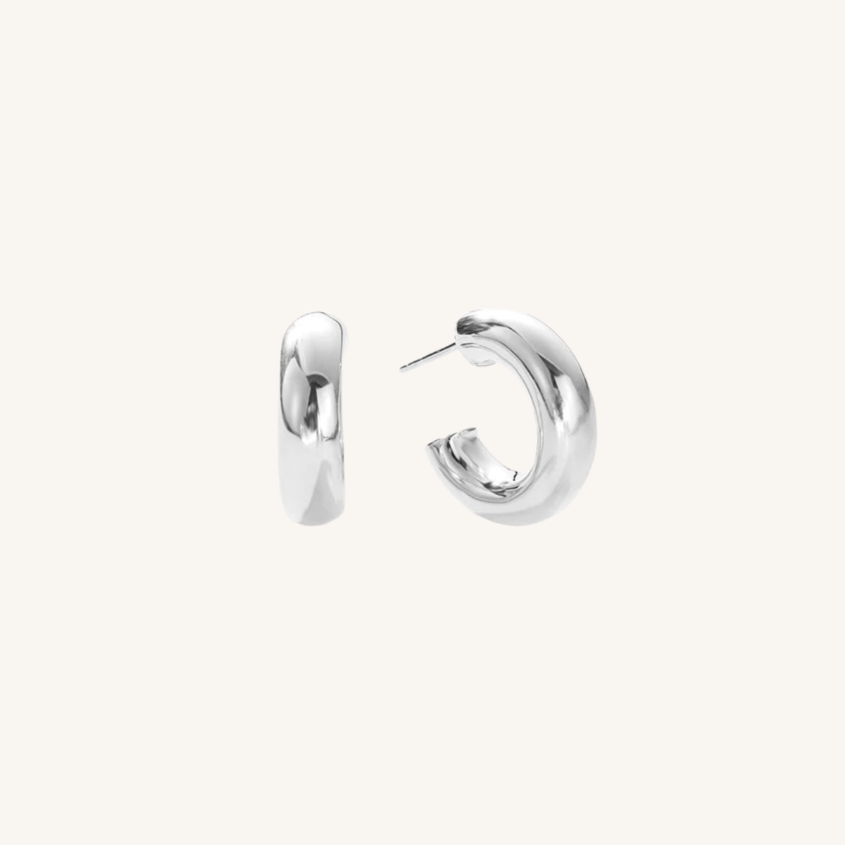 A pair of polished silver huggie hoop earrings shown from the side and back on a light cream background.