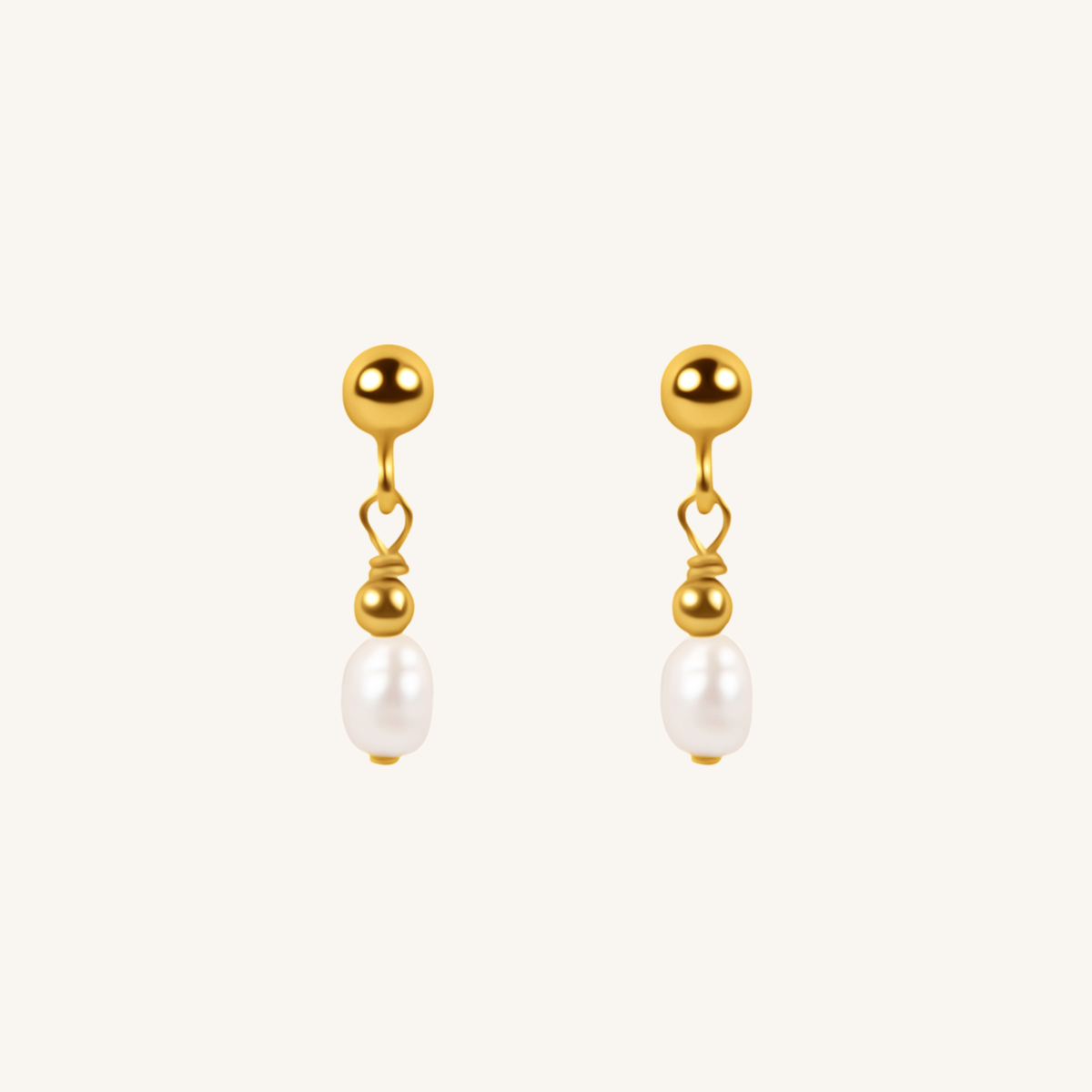 A pair of gold dangle earrings with a small heart-shaped wire detail and a white pearl drop, shown on a light cream background.