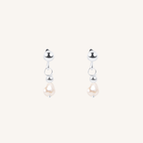 A pair of silver dangle earrings with a small silver bead, a tiny silver hoop, and a teardrop-shaped white pearl hanging below, set against a solid off-white background.