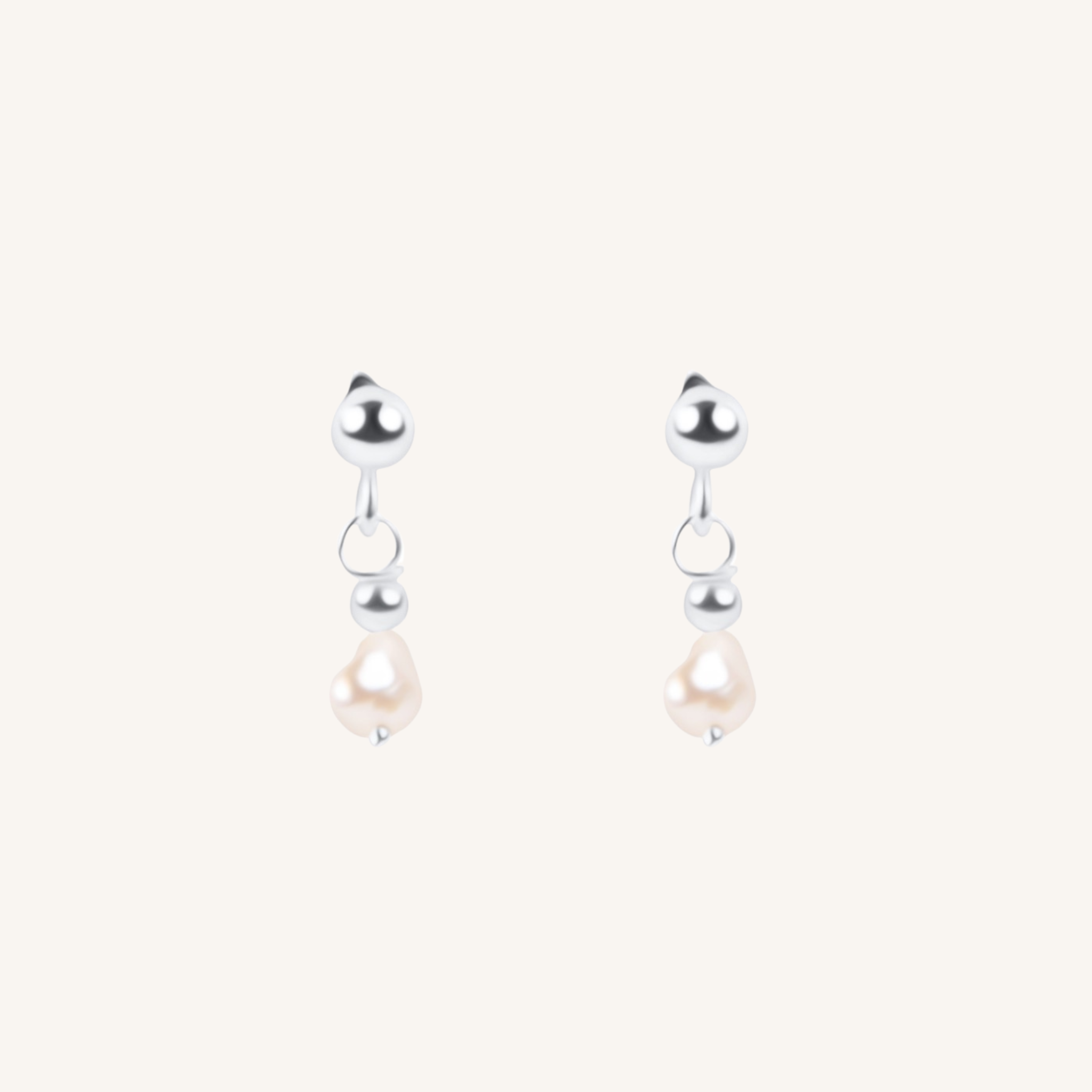 A pair of silver dangle earrings with a small silver bead, a tiny silver hoop, and a teardrop-shaped white pearl hanging below, set against a solid off-white background.