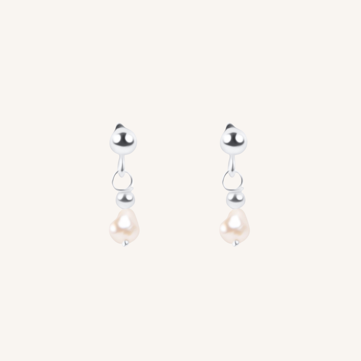A pair of silver dangle earrings with a small silver bead, a tiny silver hoop, and a teardrop-shaped white pearl hanging below, set against a solid off-white background.