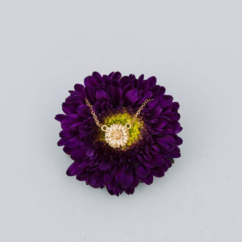 Gold necklace displayed on a purple flower with a light gray background