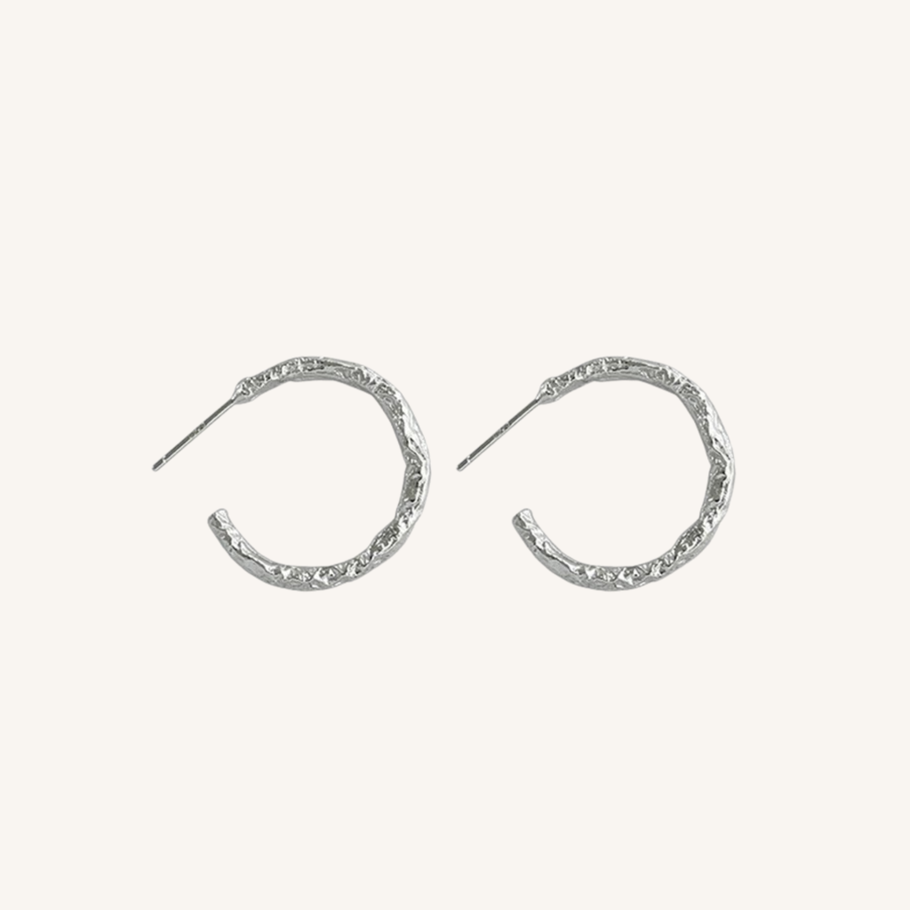 A pair of textured silver crescent hoop earrings with post backs, displayed on a clean off-white background.