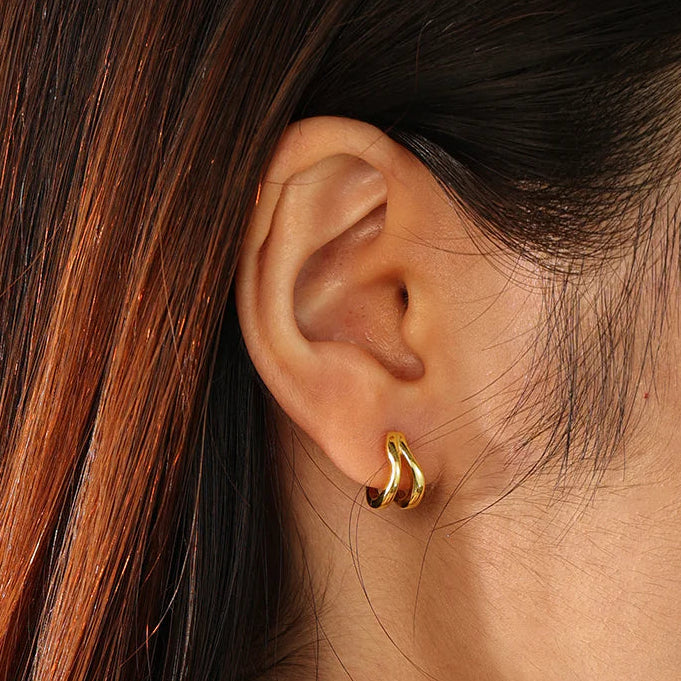 Close-up of an ear wearing a gold hoop earring with hair partially obscuring the view.