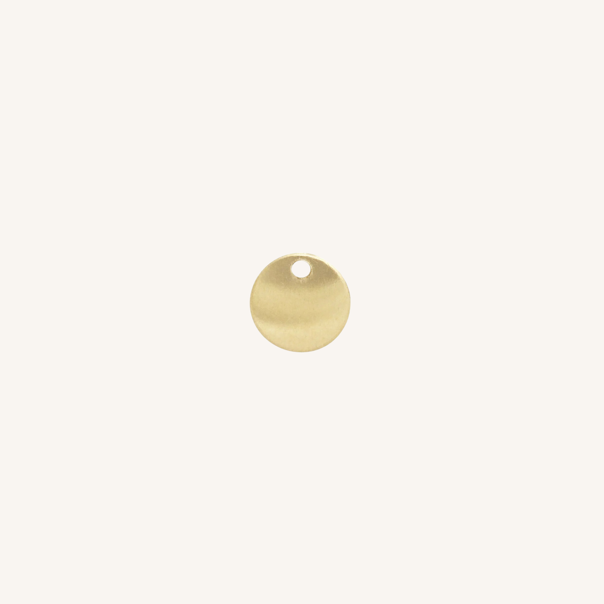 A small round gold disc charm with a hole at the top, centered on a plain off-white background.