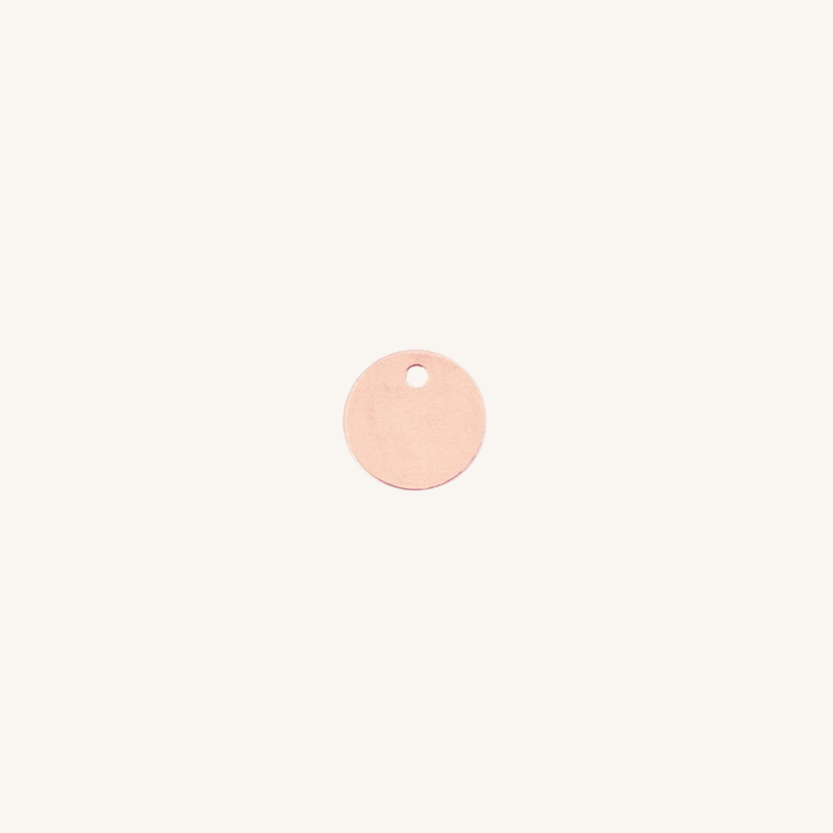 A small round rose gold disc charm with a hole at the top, centered on a plain off-white background.