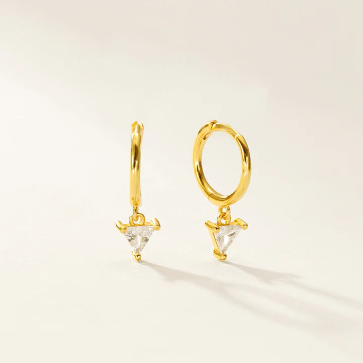 A pair of gold huggie hoop earrings with small triangular clear crystal charms, displayed on a clean off-white background.
