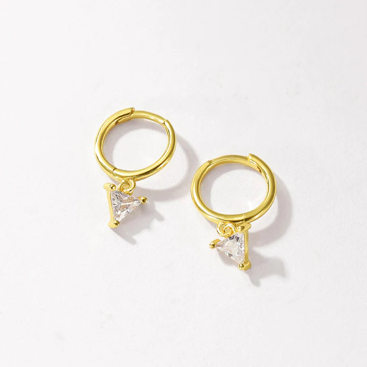A pair of gold huggie hoop earrings with small triangular clear crystal charms, displayed on a clean off-white background.