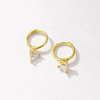 A pair of gold huggie hoop earrings with small triangular clear crystal charms, displayed on a clean off-white background.