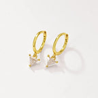 A pair of gold huggie hoop earrings with small triangular clear crystal charms, displayed on a clean off-white background.