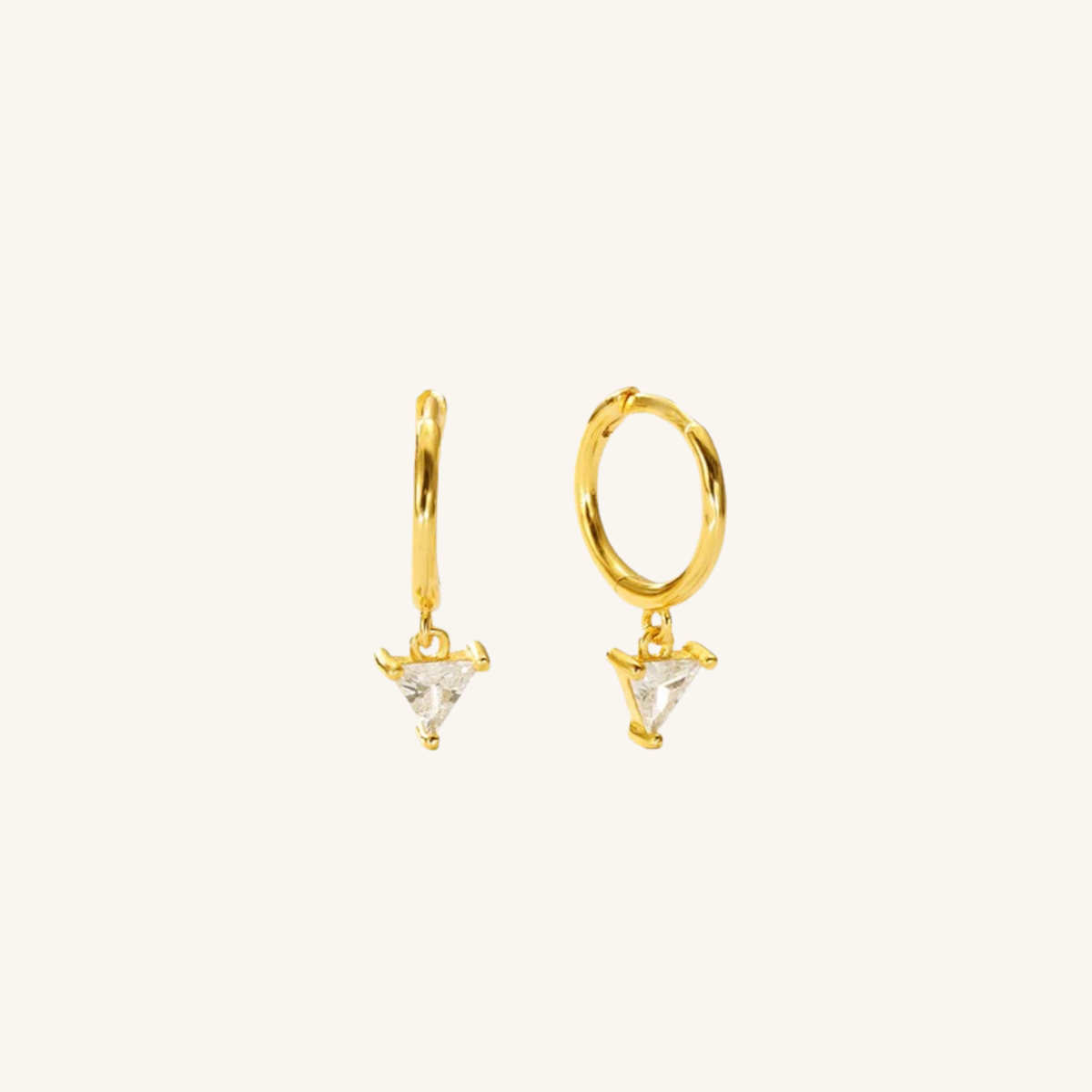 A pair of gold huggie hoop earrings with small triangular clear crystal charms, displayed on a clean off-white background.