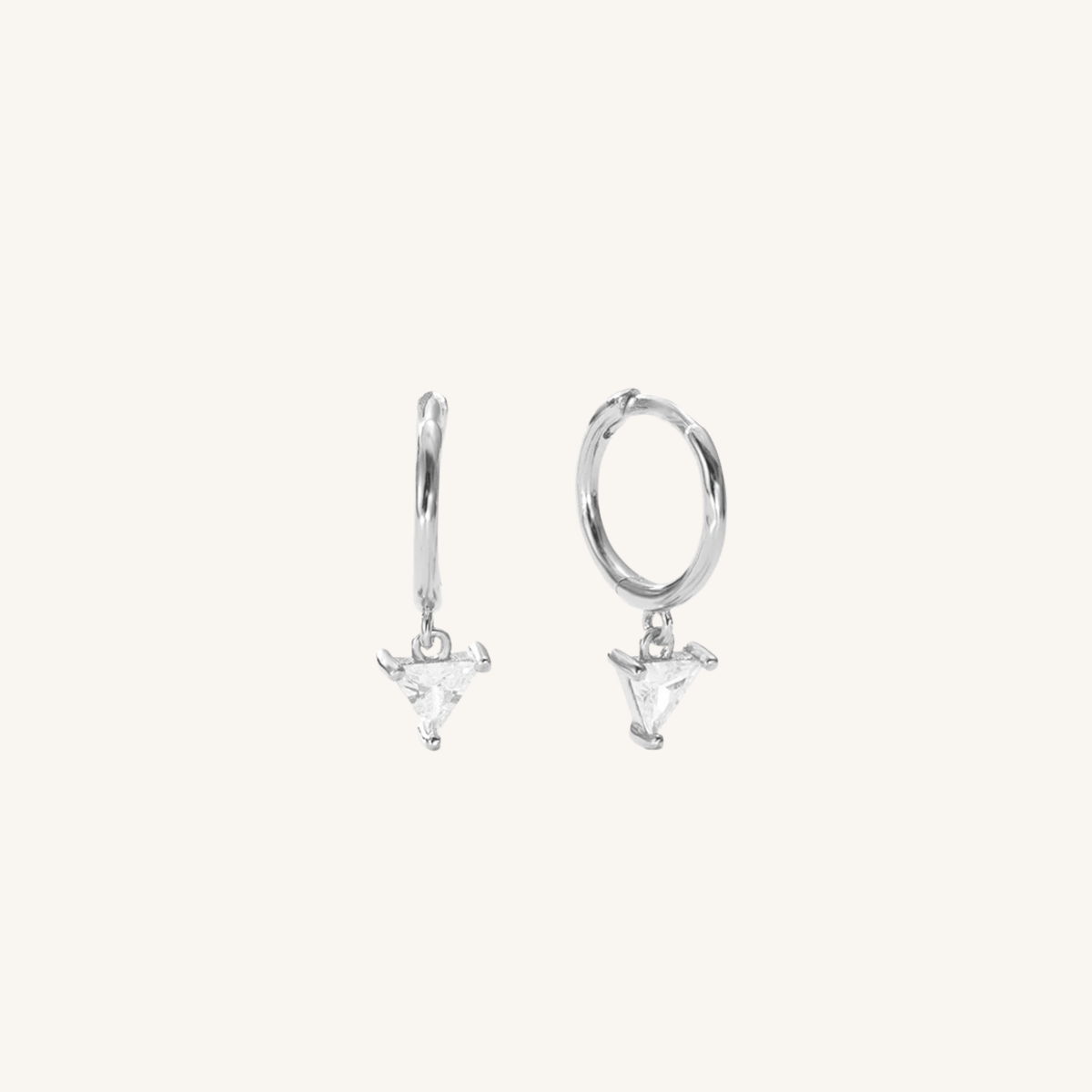 A pair of silver huggie hoop earrings with dangling triangular charms, shown on a plain off-white background.