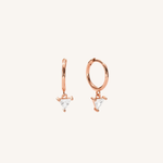 A pair of rose gold huggie hoop earrings with small triangular clear crystal drops, shown on a solid off-white background.