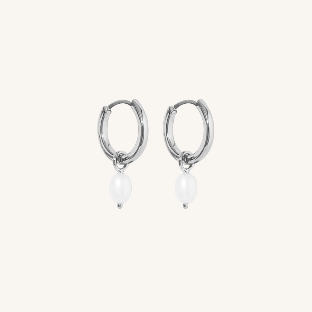Silver hoop earrings with white pearls on a light beige background