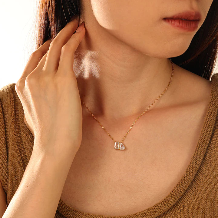 Model wearing a delicate gold chain necklace with a small pendant featuring two marquise-cut clear gemstones in a gold setting, displayed against a solid off-white background.