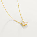 A delicate gold chain necklace with a small pendant featuring two marquise-cut clear gemstones in a gold setting, displayed against a solid off-white background.