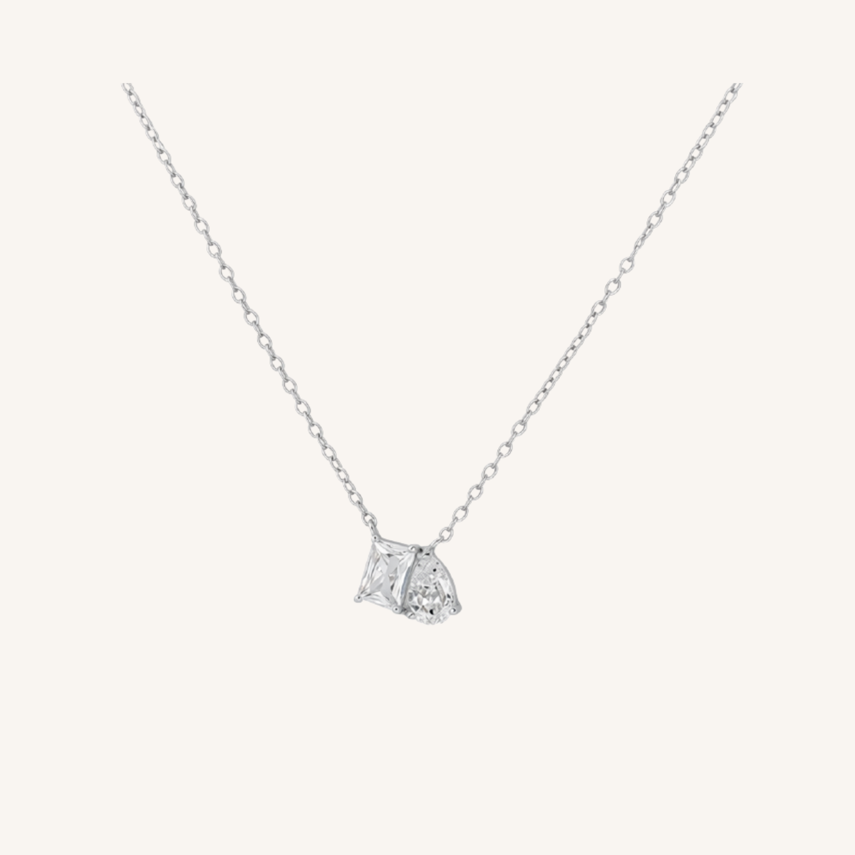 A delicate silver chain necklace with a small geometric diamond pendant, displayed on a clean off-white background.