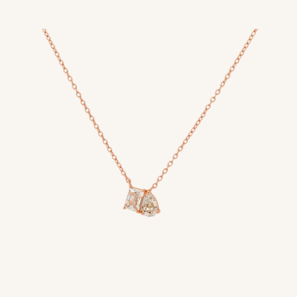 A delicate rose gold chain necklace with a small pendant featuring two clear gemstones in a rose gold setting, displayed against a solid off-white background.