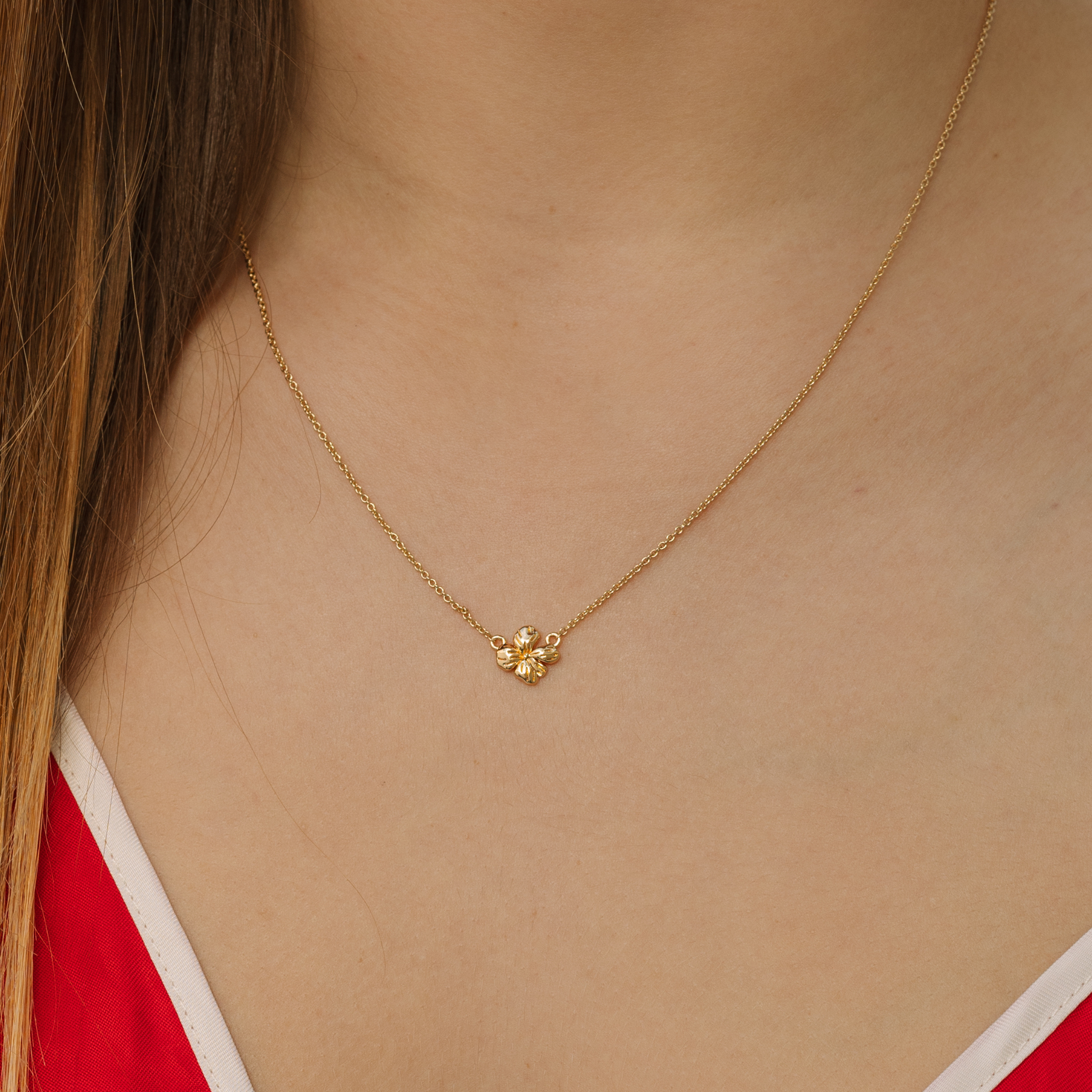 Gold necklace with a small flower pendant on a person wearing a red top.
