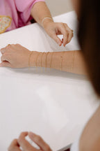 Close-up of a person's arm with gold arm cuffs on a white surface.