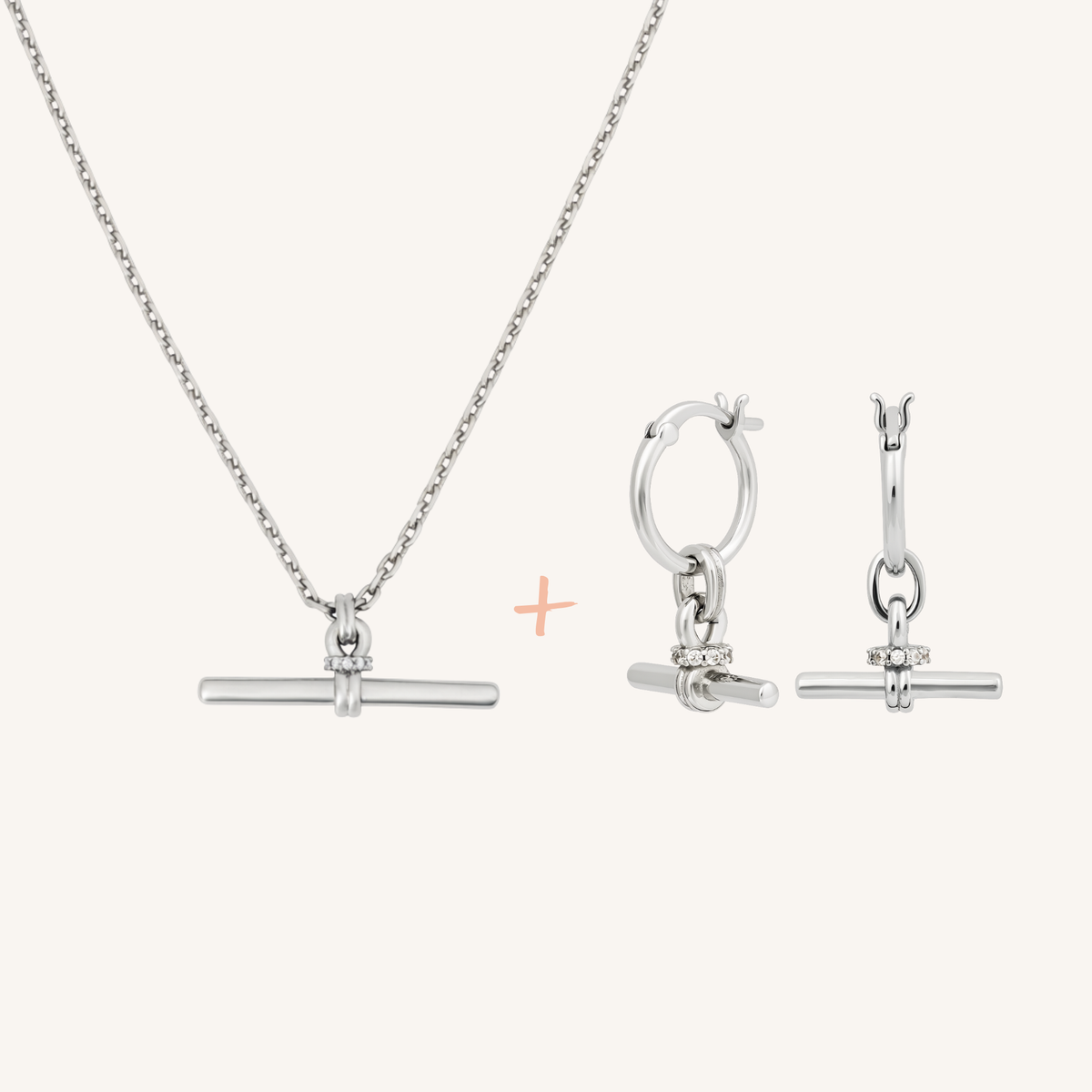 Silver jewelry set featuring a necklace with a horizontal bar pendant, matching huggie hoop earrings with a small clear gemstone accent, and a small peach plus sign between the items, shown on a light cream background.
